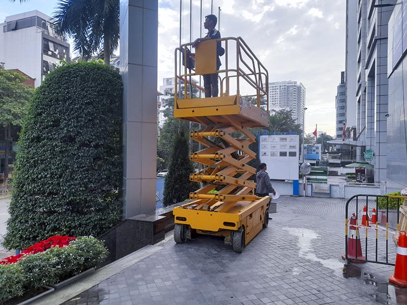 công nhân lái xe nâng người cắt kéo bảo trì toà nhà