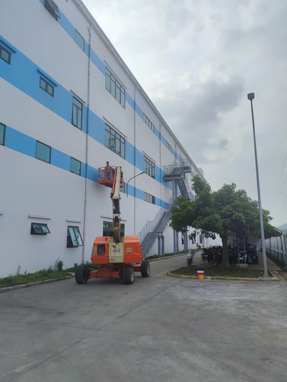 công nhân lái xe nâng người boomlift sơn lại nhà máy