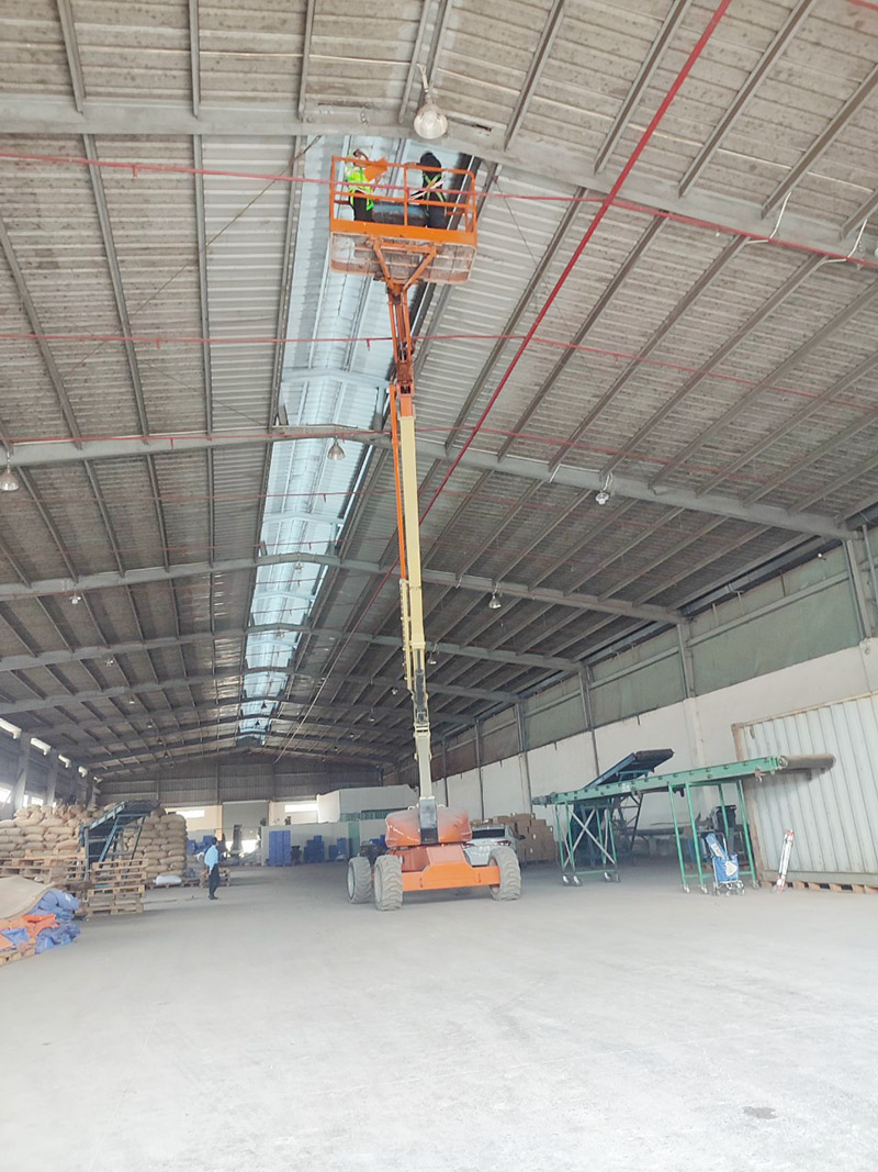công nhân vận hành xe nâng người boomlift thay bóng đèn trong nhà xưởng
